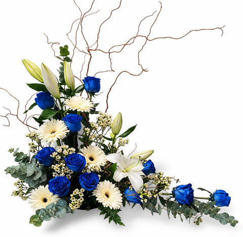 Arrangement funéraire Élégance Boréale avec roses bleues, germinis blancs, lys blancs, wax flower, eucalyptus et branches naturelles décoratives.
