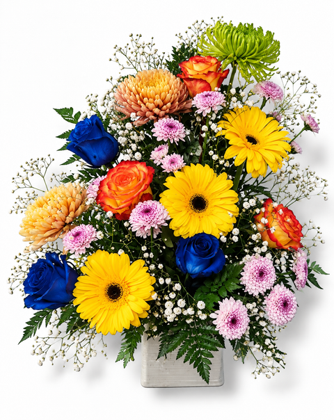 Bouquet multicolore en hauteur dans un contenant carré blanc, composé de gerberas jaunes, de roses orange et bleues, de chrysanthèmes dorés et verts, de mini-marguerites mauves et de gypsophile.