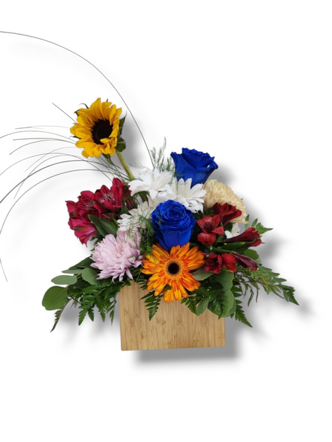 Arrangement floral coloré dans boîte de bois avec rose bleue, tournesol, gerbera orange, marguerites blanches, alstroemerias et feuillage.