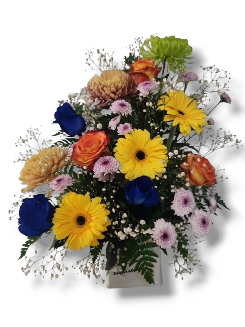 Bouquet vertical avec roses bleues, gerberas jaunes, chrysanthèmes dorés, marguerites mauves et feuillage dans un vase blanc.