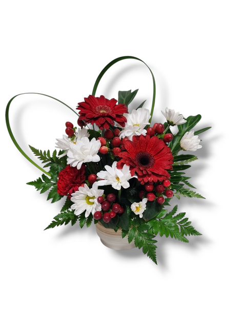 Arrangement floral rouge et blanc avec gerberas, marguerites, baies rouges et feuillage en cœur.