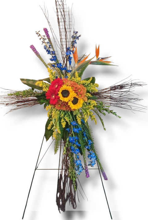 Croix funéraire florale colorée avec tournesols, gerberas rouges, delphiniums bleus et oiseaux du paradis – modèle Croix Lumière.