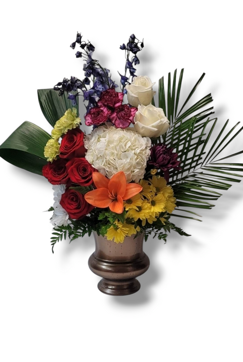 Arrangement funéraire multicolore avec lys orange, roses rouges et blanches, hydrangée, marguerites jaunes et feuillage tropical – modèle Harmonie de Couleurs.