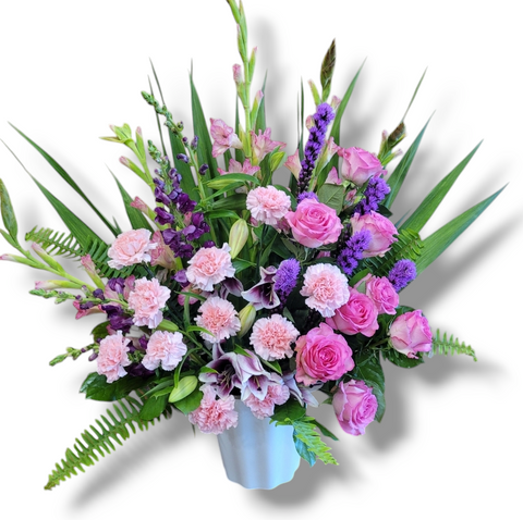 Arrangement floral mauve et rose avec roses, œillets et lisianthus dans un vase argenté.