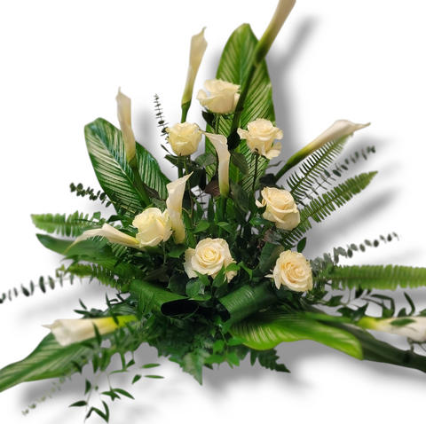 Arrangement funéraire avec callas et roses ivoire dans un style moderne et feuillage tropical.
