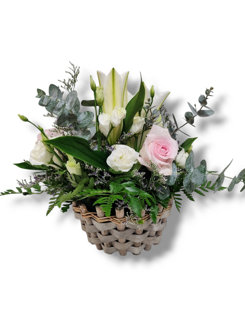 Arrangement floral pastel dans panier tressé avec lys blancs, roses pâles, lisianthus crème et eucalyptus.