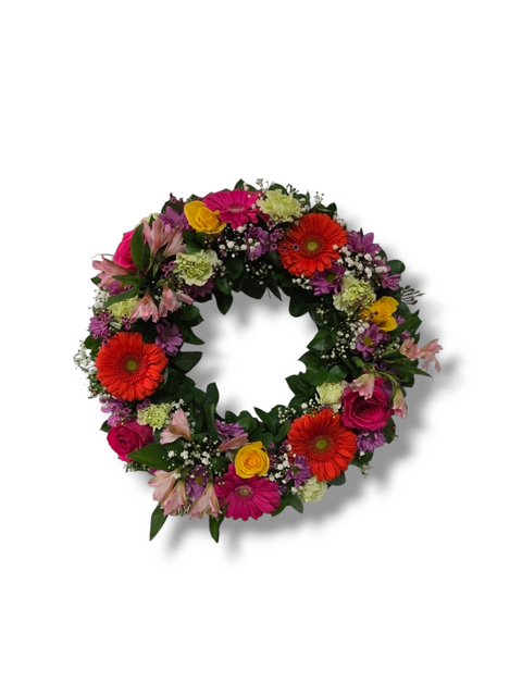 Couronne funéraire florale colorée avec gerberas, roses, alstroemerias et feuillage – hommage vibrant à la vie.