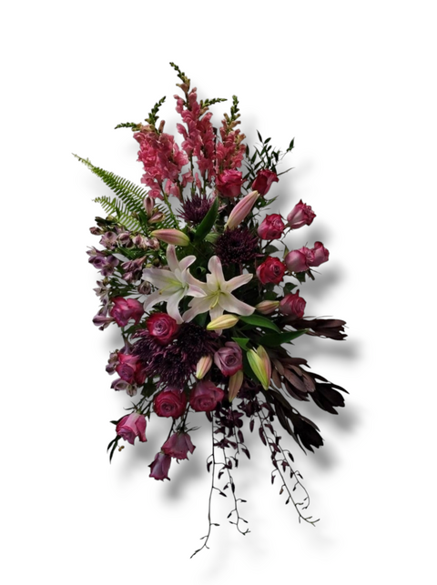 Gerbe funéraire verticale avec lys blancs, roses mauves, chrysanthèmes bordeaux et feuillage, montée sur support.
