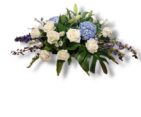 Coussin de cercueil Bleu Sérénité avec roses blanches, hortensias bleus, lys et feuillage tropical – arrangement funéraire horizontal.