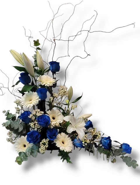 Arrangement funéraire asymétrique avec roses bleues, germinis blancs, lys, wax flower, eucalyptus et branches naturelles – modèle Élégance Boréale.
