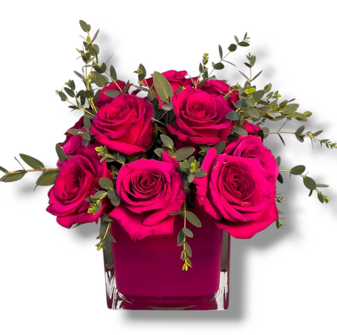 Arrangement moderne avec roses fuchsia dans vase carré en verre, accompagné de feuillage discret – style chic et intense.