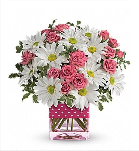 Arrangement de marguerites blanches et mini roses roses dans un vase carré rose à pois blancs.