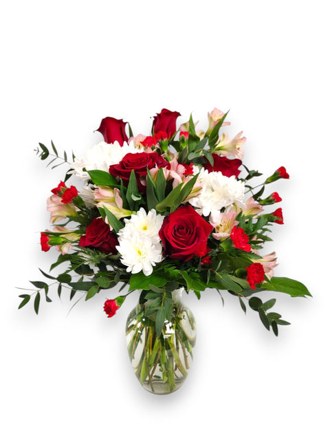 Bouquet de roses rouges, marguerites blanches et alstroemerias dans un vase transparent.

