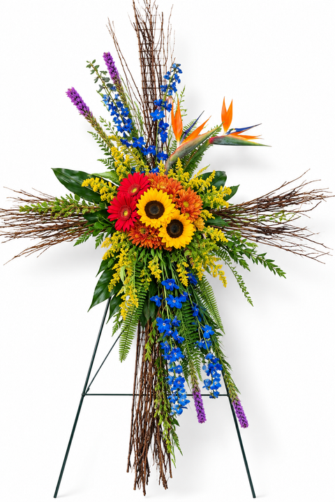 Croix funéraire florale montée sur chevalet, composée de tournesols, gerberas rouges, solidago jaune, delphiniums bleus, oiseau du paradis et feuillage tropical.