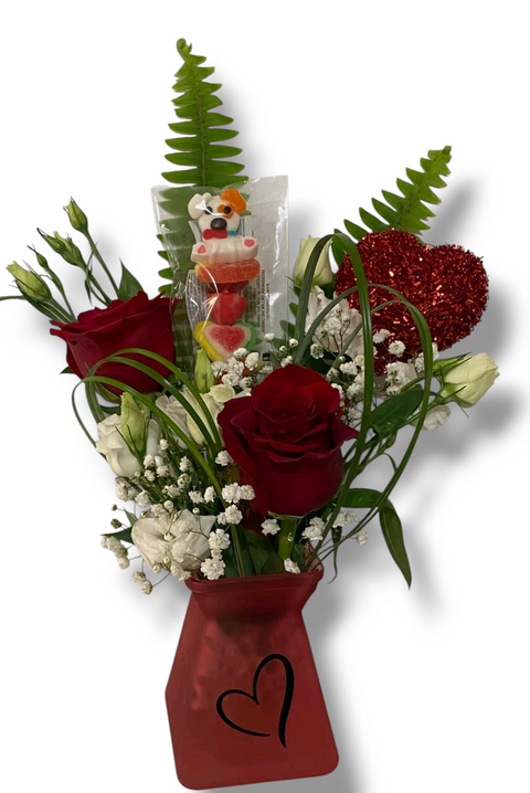 Arrangement  avec roses rouges, fleurs blanches, cœur rouge pailleté et brochette de bonbons Laura Secord, dans un vase rouge avec cœur.