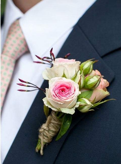 Boutonnière avec rose rose et boutons de roses pastel nouée avec ficelle naturelle sur veston foncé.

