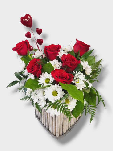 Arrangement floral en forme de cœur avec roses rouges et marguerites blanches dans un contenant en bois