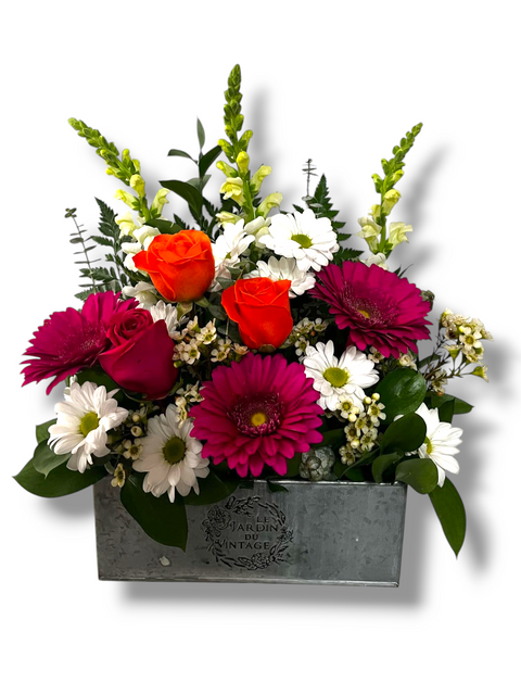 Arrangement floral dans boîte vintage avec roses orange, gerberas fuchsia, marguerites blanches et feuillage décoratif.