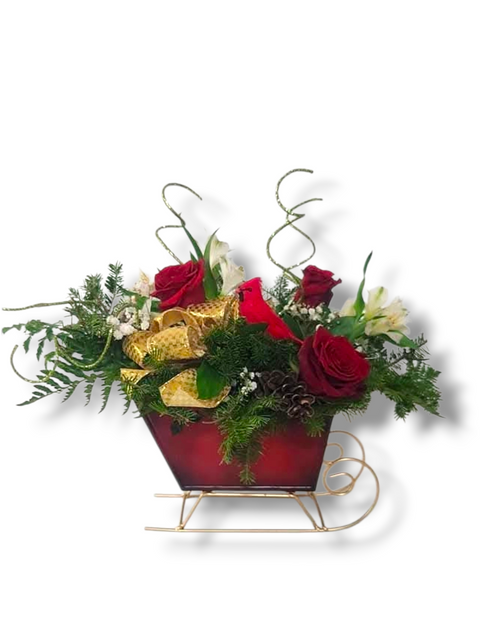 Arrangement floral de Noël avec roses rouges, fleurs blanches, ruban doré et sapinage dans un traîneau rouge en métal doré – modèle « Traîneau de Noël Éclatant » par Fleur de Guy.