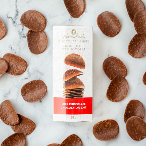 Boîte de croustilles de chocolat au lait Laura Secord entourée de morceaux de chocolat sur fond de marbre blanc.

